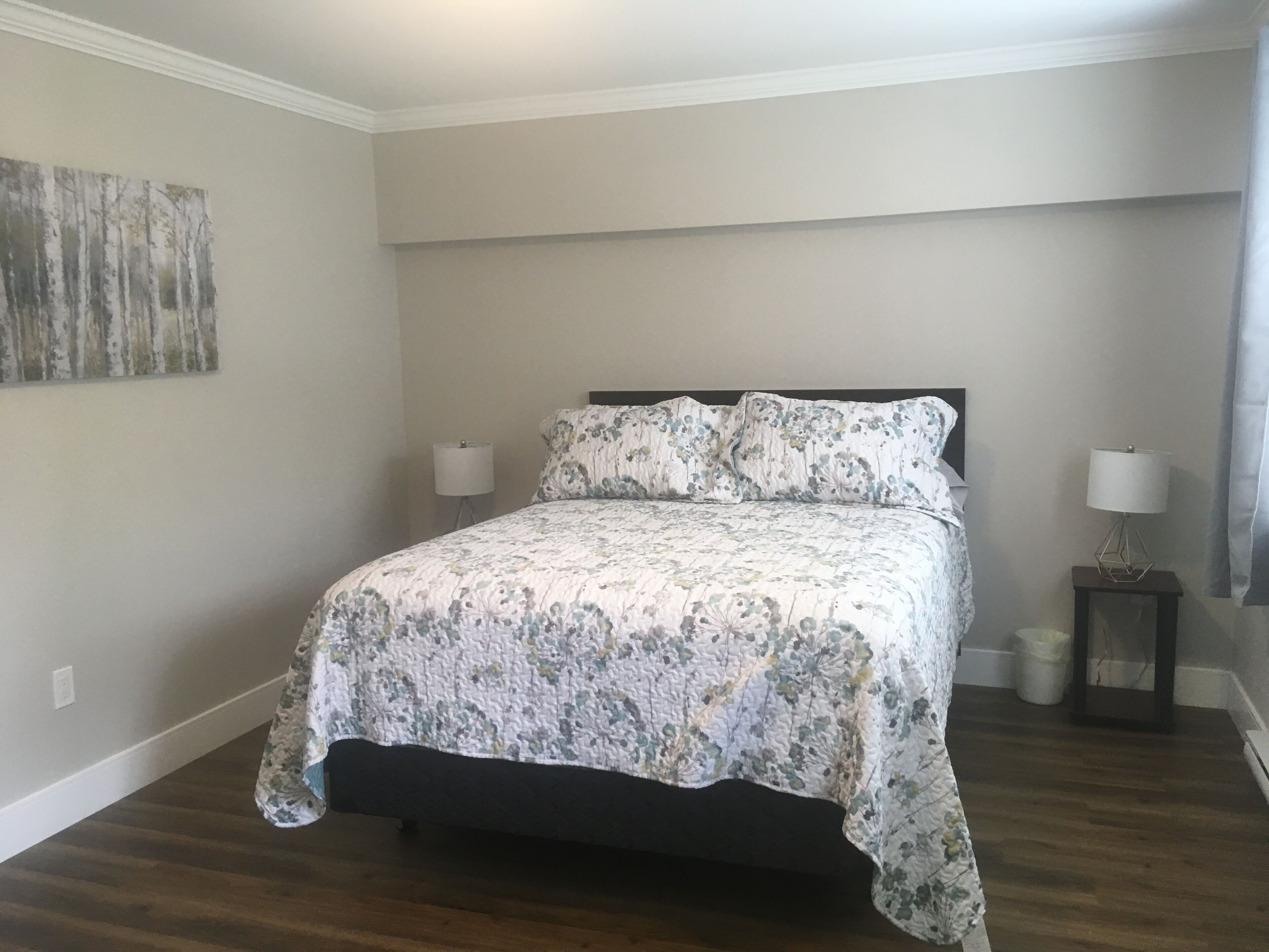 A bedroom with a bed, two bedside tables, a wall-mounted lamp, and a painting.