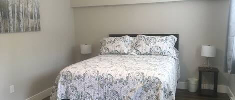 A bedroom with a bed, two bedside tables, a wall-mounted lamp, and a painting.