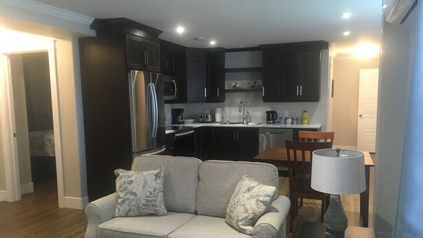 Ein modernes Wohnzimmer mit grauem Sofa, einem Esstisch und einer Küche im Hintergrund.