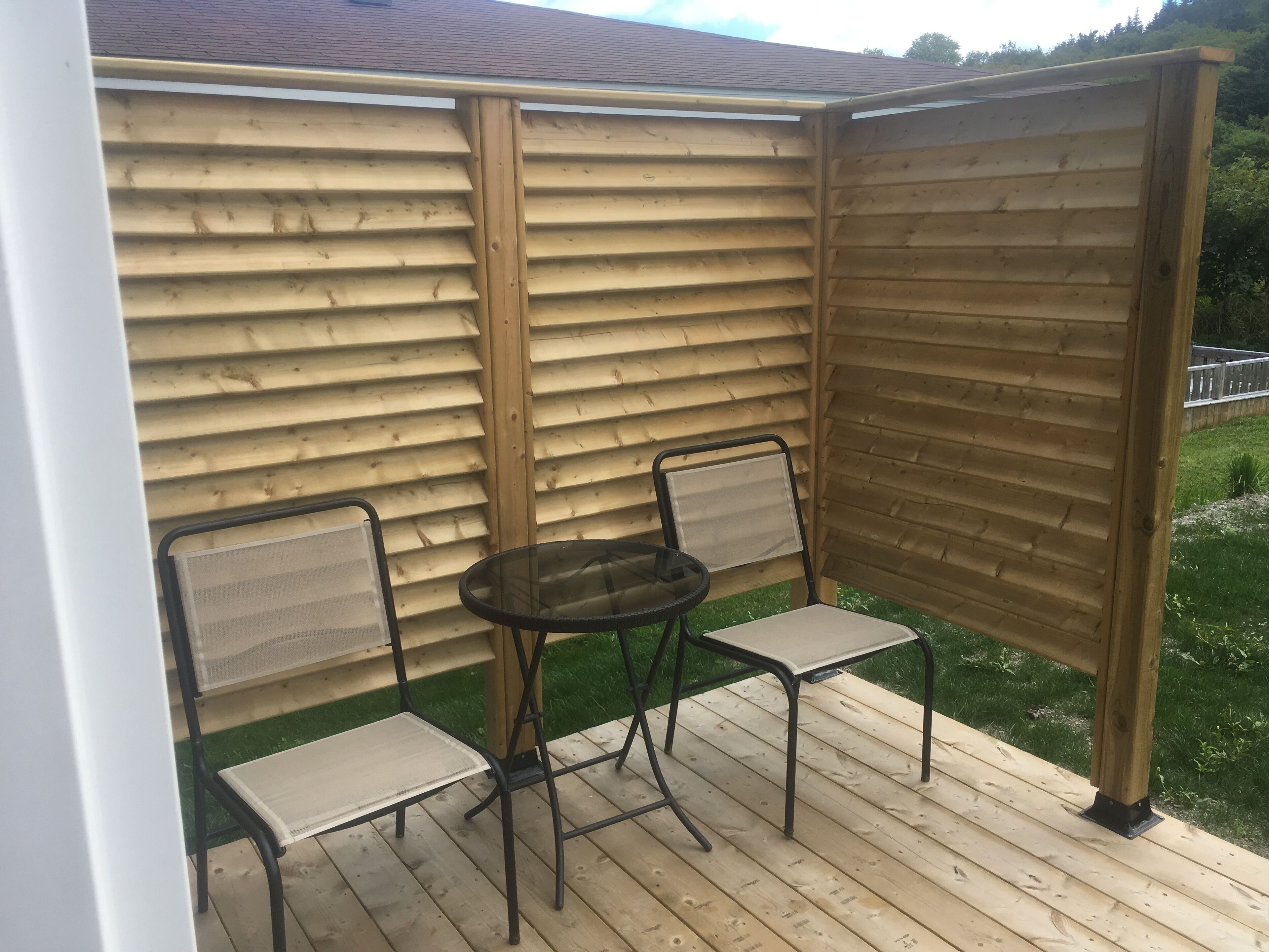 A wooden deck with two chairs and a table, surrounded by a wooden fence.