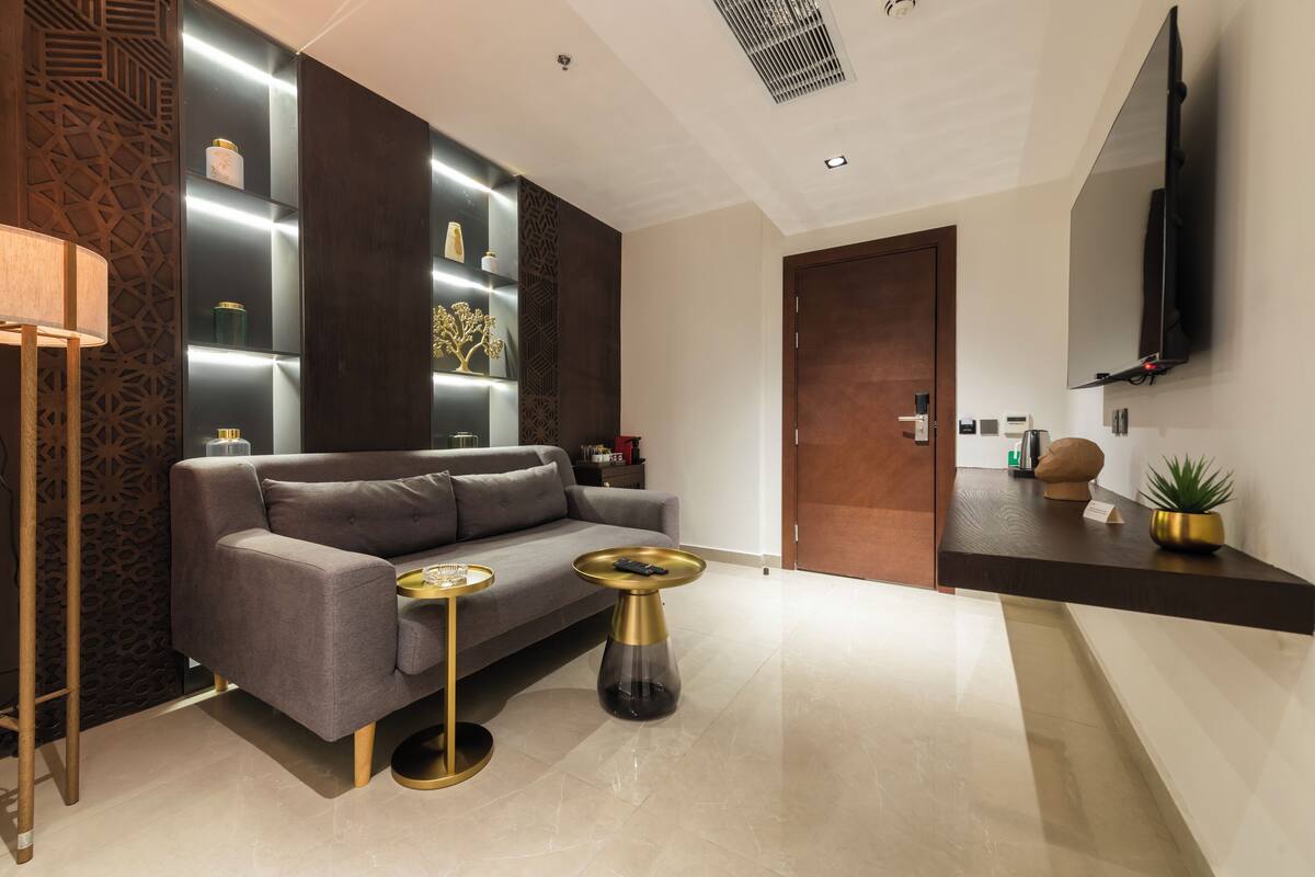 A modern living room with a grey sofa, a gold and black side table, and a wall-mounted TV.