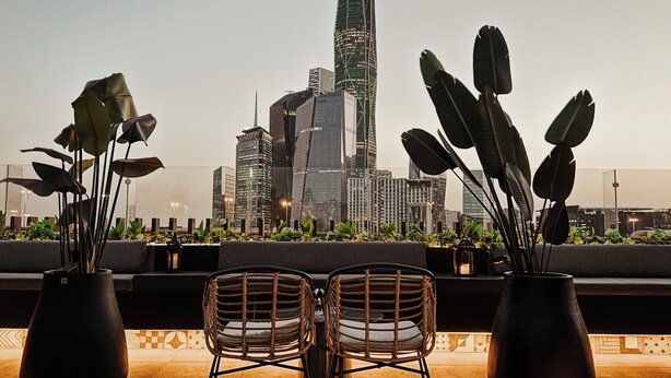 A rooftop terrace with two wicker chairs, potted plants, and a city skyline view. - Tajreed Hotel (Riyadh)