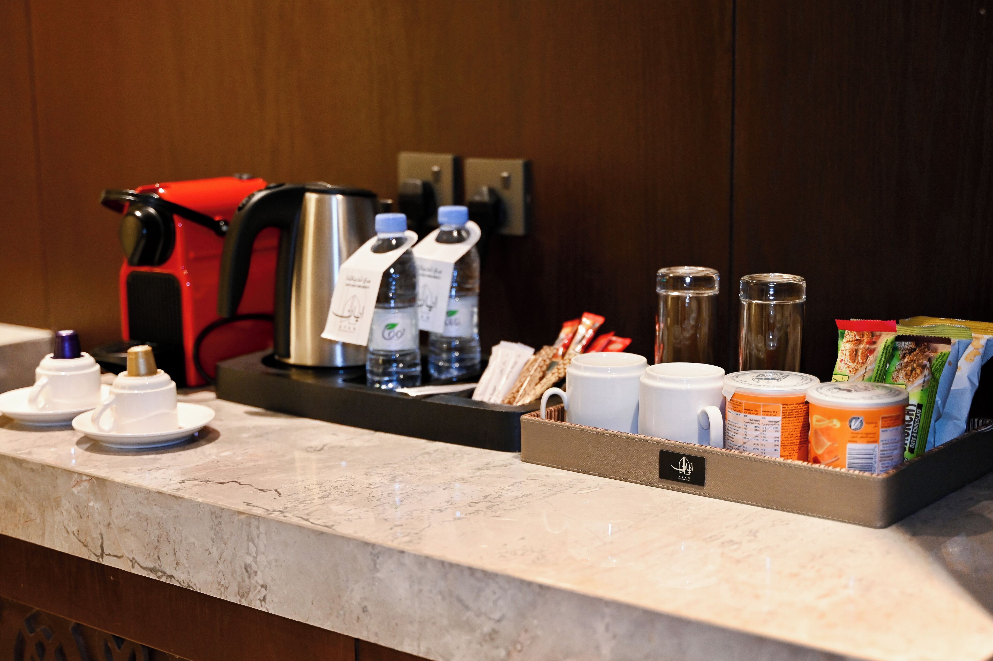 Ein Frühstücksbuffet in einem Hotelzimmer mit Kaffeemaschine, Wasserflaschen, Tassen und verpackten Lebensmitteln.