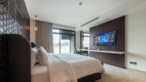 A modern hotel room with a large bed, a flat-screen TV mounted on the wall, a desk, and a view of the city through large windows. - Tajreed Hotel (Riyadh)