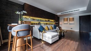 A modern living room with a white sofa, blue and yellow cushions, wooden chairs, a coffee table, and a decorative shelf with various items. - Tajreed Hotel (Riyadh)