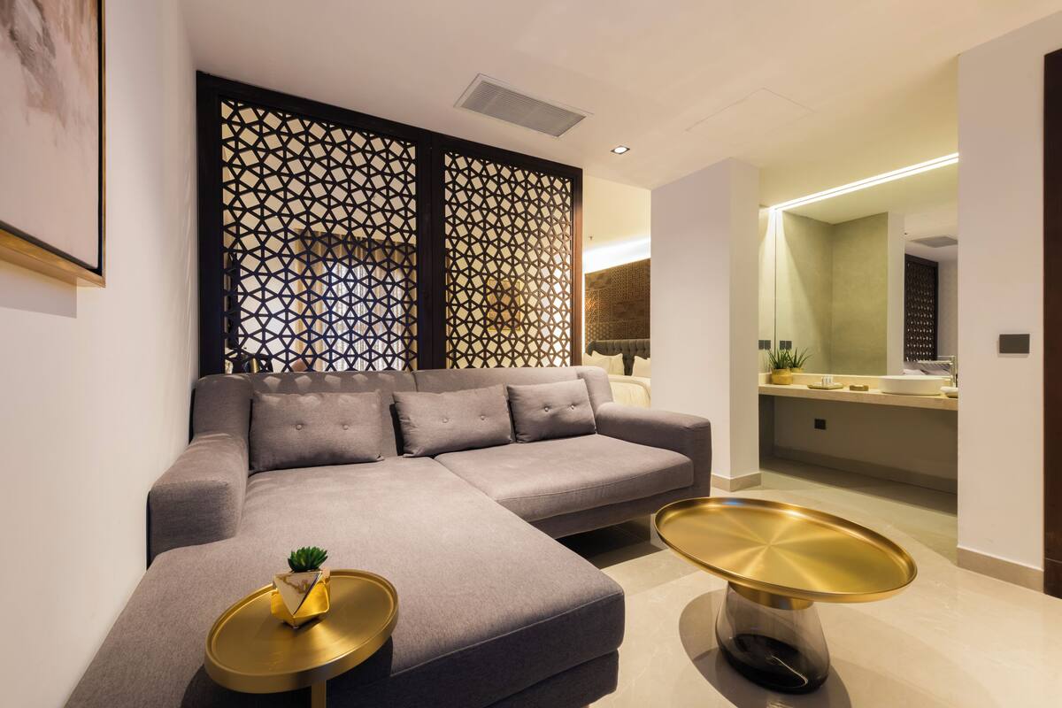 A modern living room with a grey sectional sofa, two gold side tables, and a decorative wall panel.