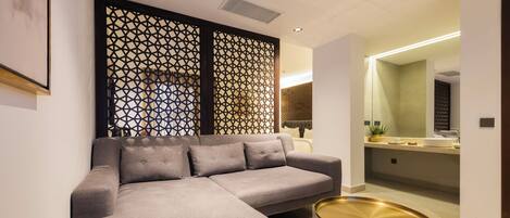 A modern living room with a grey sectional sofa, two gold side tables, and a decorative wall panel.