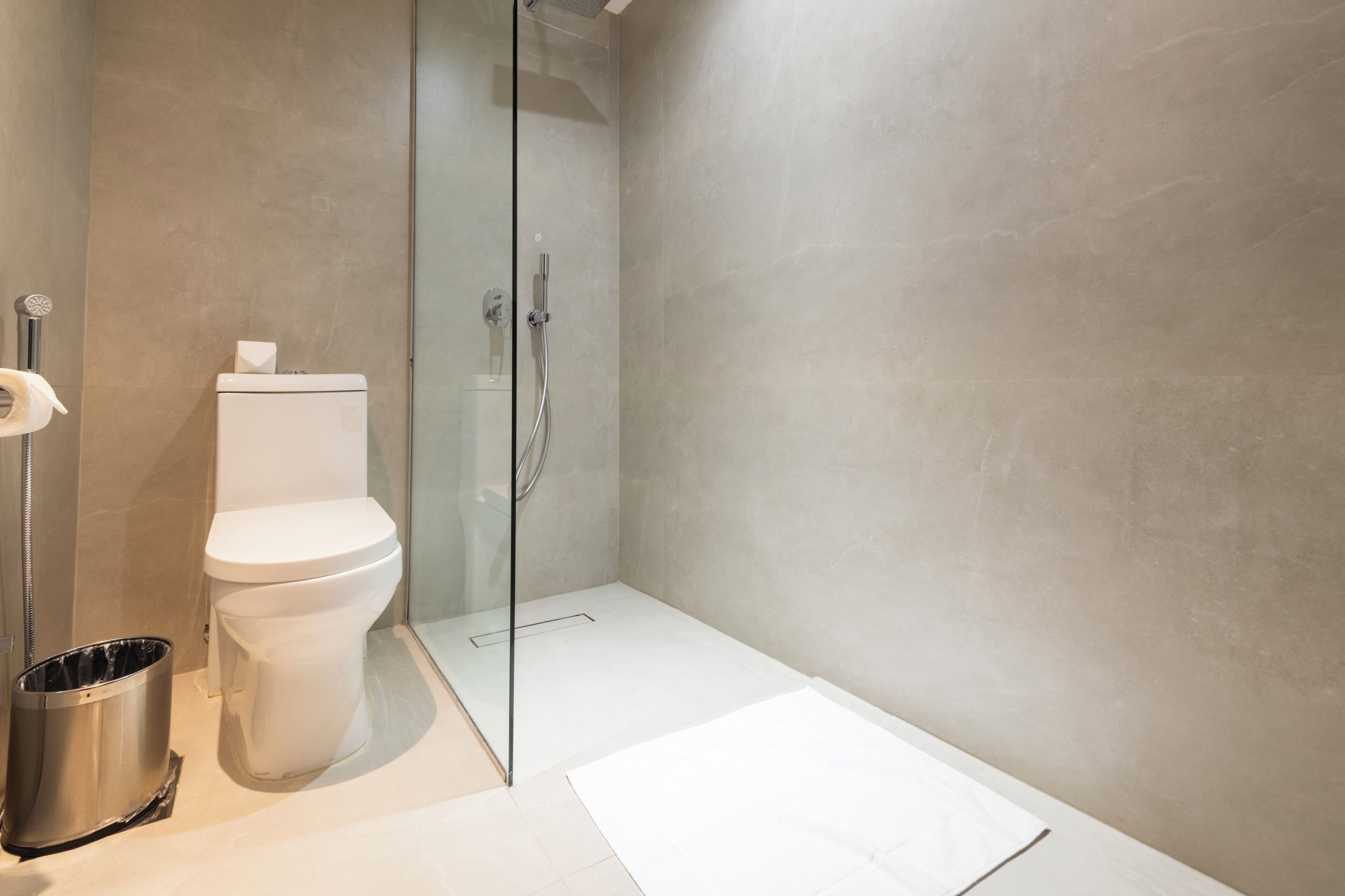Een moderne badkamer met een glazen douchecabine, een toilet en een prullenbak.