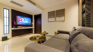A modern living room with a large flat-screen TV, a sofa, and two small round tables. - Tajreed Hotel (Riyadh)