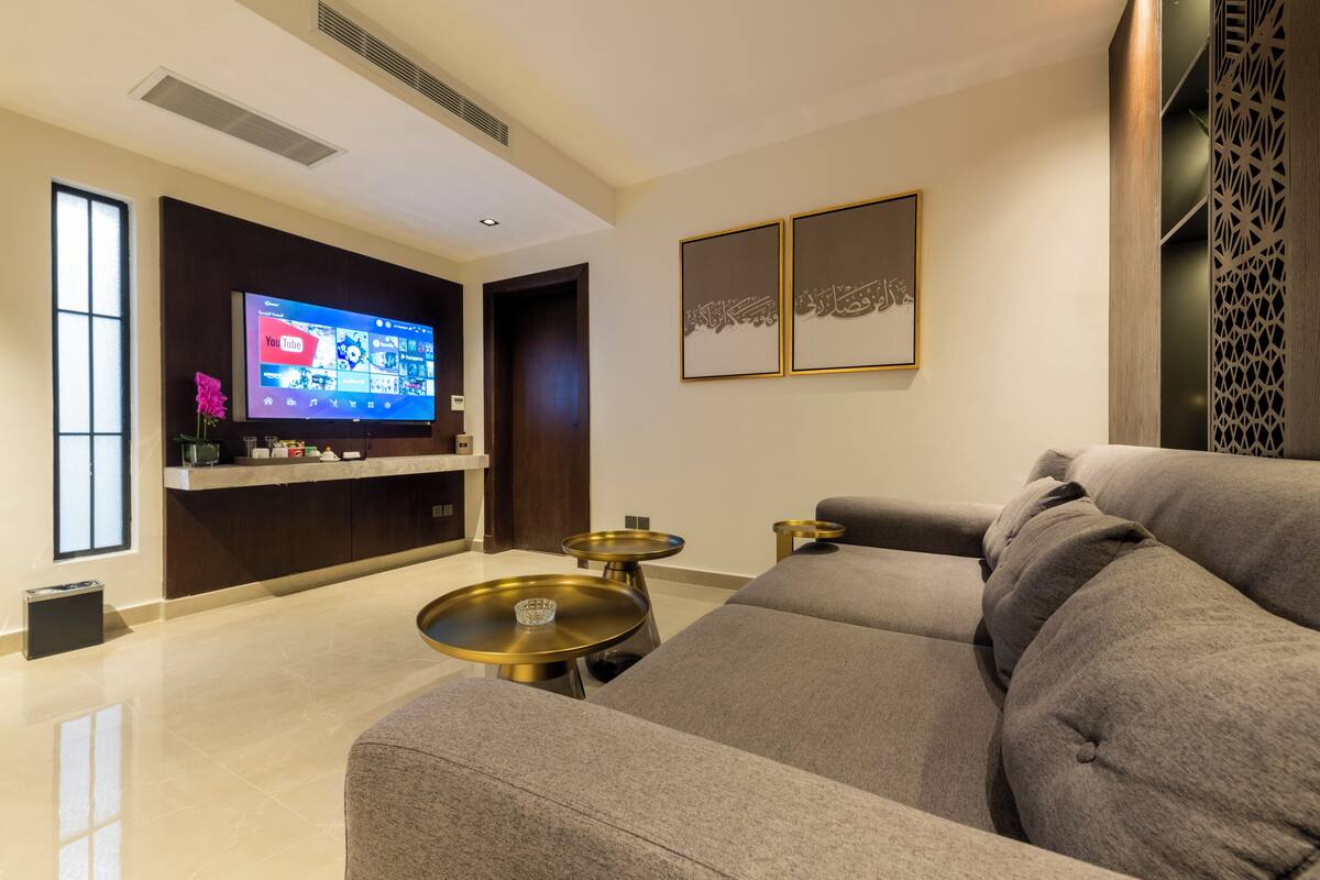 A modern living room with a large flat-screen TV, a sofa, and two small round tables.