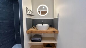 Ein Badezimmer mit einem weißen Waschbecken, einem Holz-Waschtisch und einem Spiegel mit Beleuchtung.