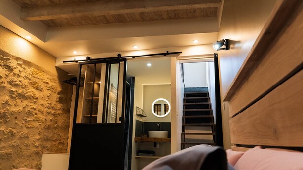 Ein Schlafzimmer mit einem Bett, einem hölzernen Kopfteil, einer Steinwand, einer Schiebetür zu einem Badezimmer und einem runden Spiegel über dem Waschbecken.