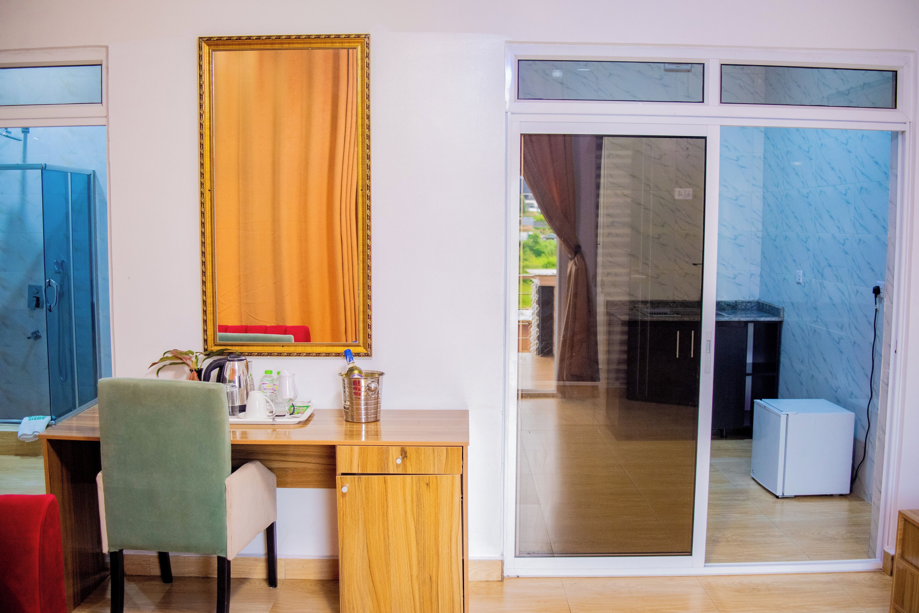 A room with a wooden desk, a chair, a small cabinet, a mirror, and a sliding glass door leading to a balcony.