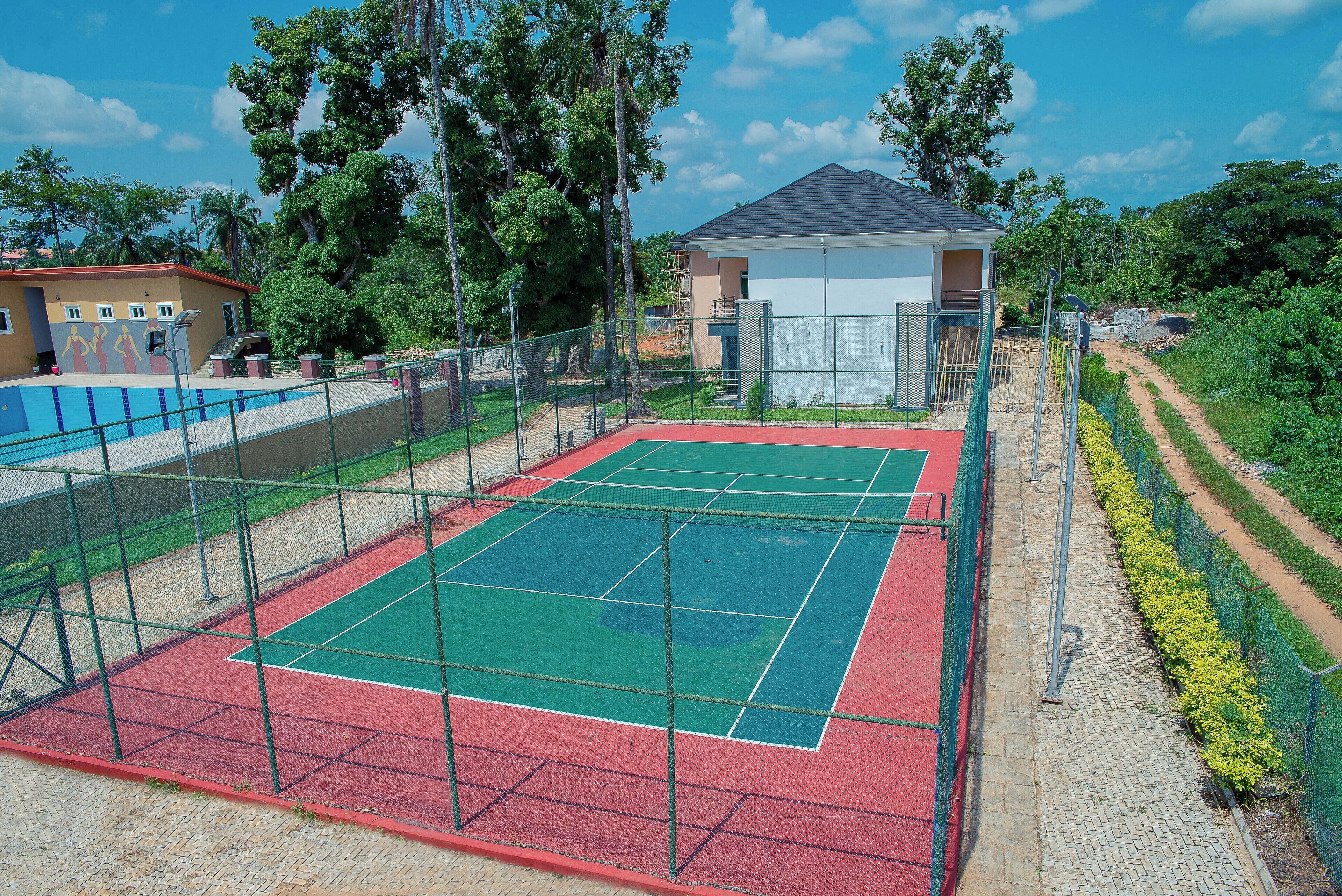 An outdoor tennis court with a net, surrounded by a fence and a small building.