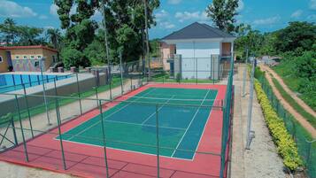 An outdoor tennis court with a net, surrounded by a fence and a small building.