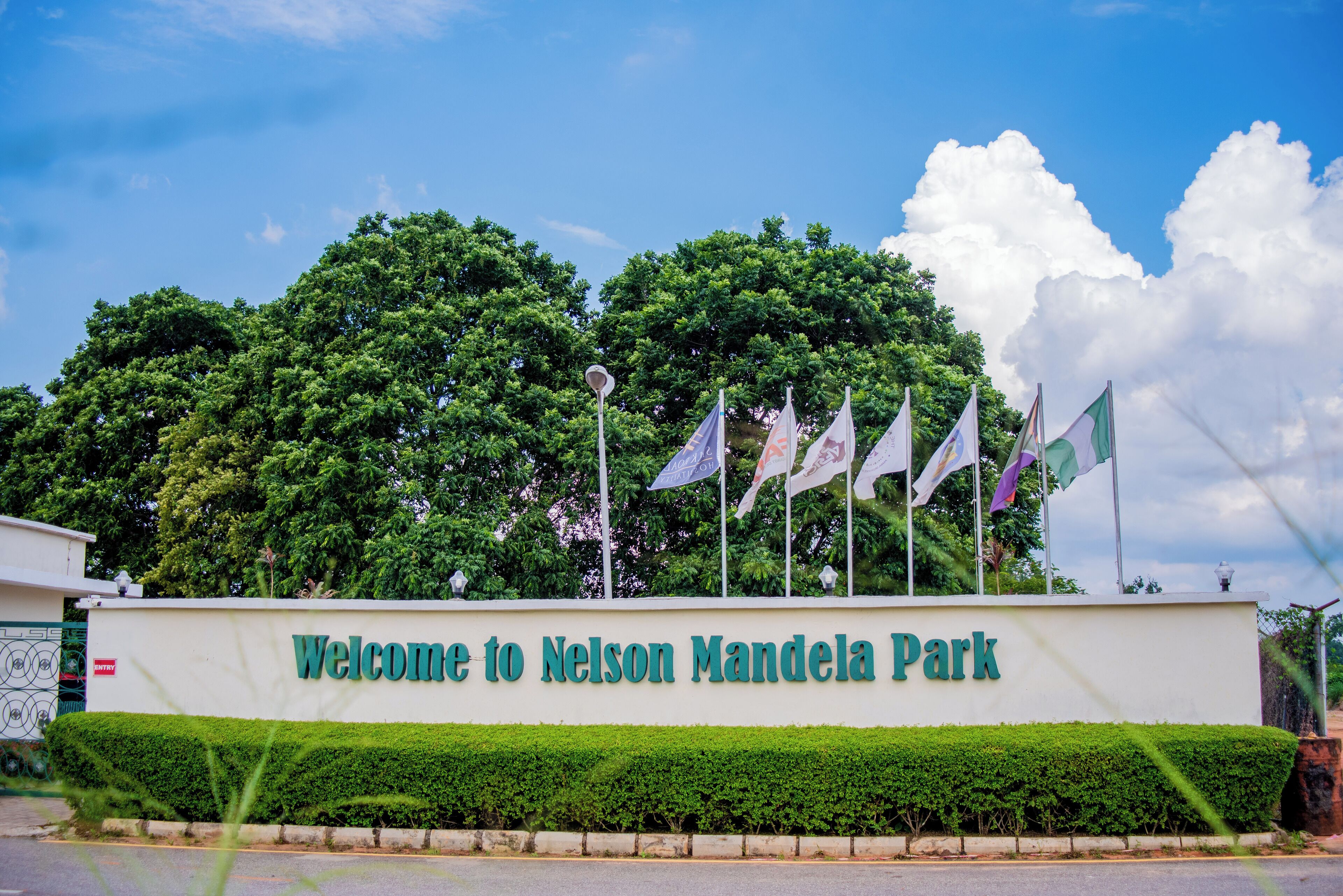 A welcome sign at Nelson Mandela Park with flags and lush greenery in the background.