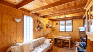 Interior de una cabaña de madera con sofá, mesa de comedor y televisor.