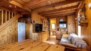 Interior de una cabaña de madera con cocina, comedor y una cama.