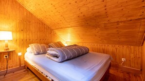 Un dormitorio con paneles de madera, una cama, almohadas, una lámpara y una mesita de noche.