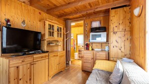 Interior de una cabaña de madera con televisión, armarios, microondas y una cama.
