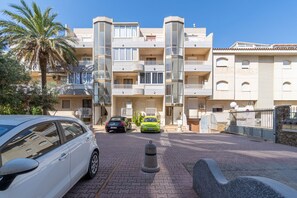 A multi-story residential building with balconies, a paved driveway, and parked cars.