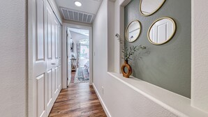 Un corridoio con porte bianche, pavimento in legno e un muro ornato da tre specchi con cornice dorata.