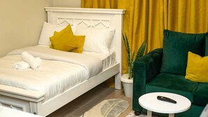 A hotel room with a bed, a green armchair, a small white table, and a potted plant. -  Modern Studio Apartment, 10- Min from JKIA Airport /SGR (Nairobi)