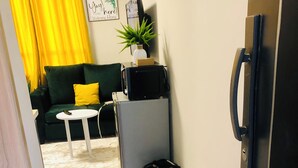 A compact living space with a green sofa, a small white table, a refrigerator, and a potted plant. -  Modern Studio Apartment, 10- Min from JKIA Airport /SGR (Nairobi)