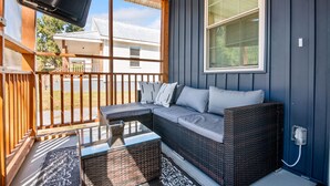 A covered porch with a wicker sofa, a glass-top table, and a TV mounted on the wall.