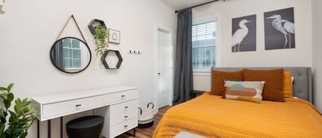 Un dormitorio moderno con un escritorio blanco, una cama grande con colcha color mostaza y dos cuadros de pájaros colgados en la pared.