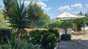 A garden pathway with a stone wall, various plants, and a white umbrella structure. - Apartment with Swimming Pool and Tennis (Montespertoli)