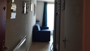 A narrow hallway with a blue sofa, a geometric light fixture, and a door on the right. - Studio 4 Personnes Avec Balcon aux Pieds des Remontées Mécaniques (Allos)