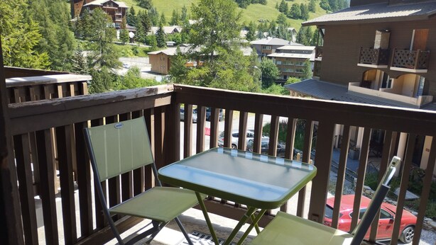 A balcony with a table and chairs, overlooking a residential area with houses and a red car in the background. - Studio 4 Personnes Avec Balcon aux Pieds des Remontées Mécaniques (Allos)