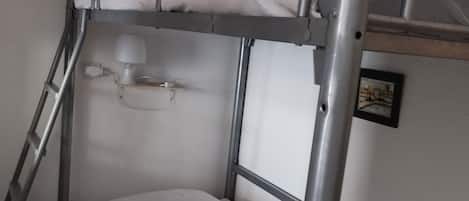 A bunk bed with a ladder, a bedside table with a lamp, and a framed picture on the wall.