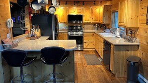 A wooden cabin-style kitchen with a central island, bar stools, a refrigerator, stove, microwave, and wooden cabinets. - Beautiful log home-dog friendly, creek & mountain views,close to national parks (MAMMOTH CREEK)