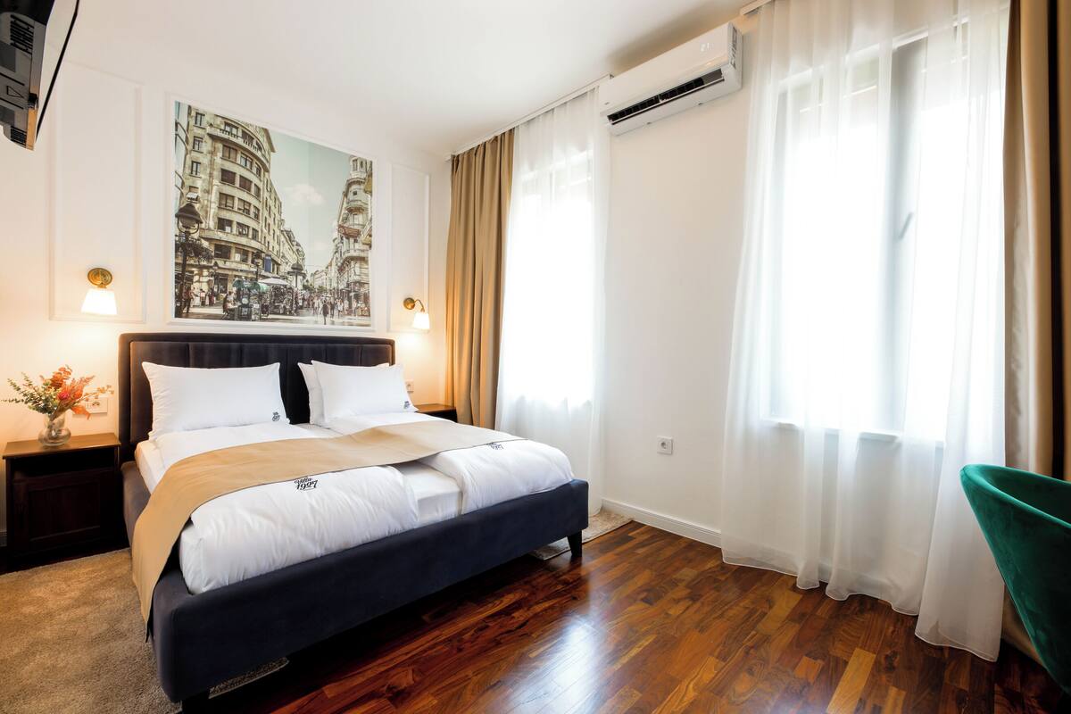 A hotel room with a bed, a nightstand, a lamp, a painting, and a window with curtains.