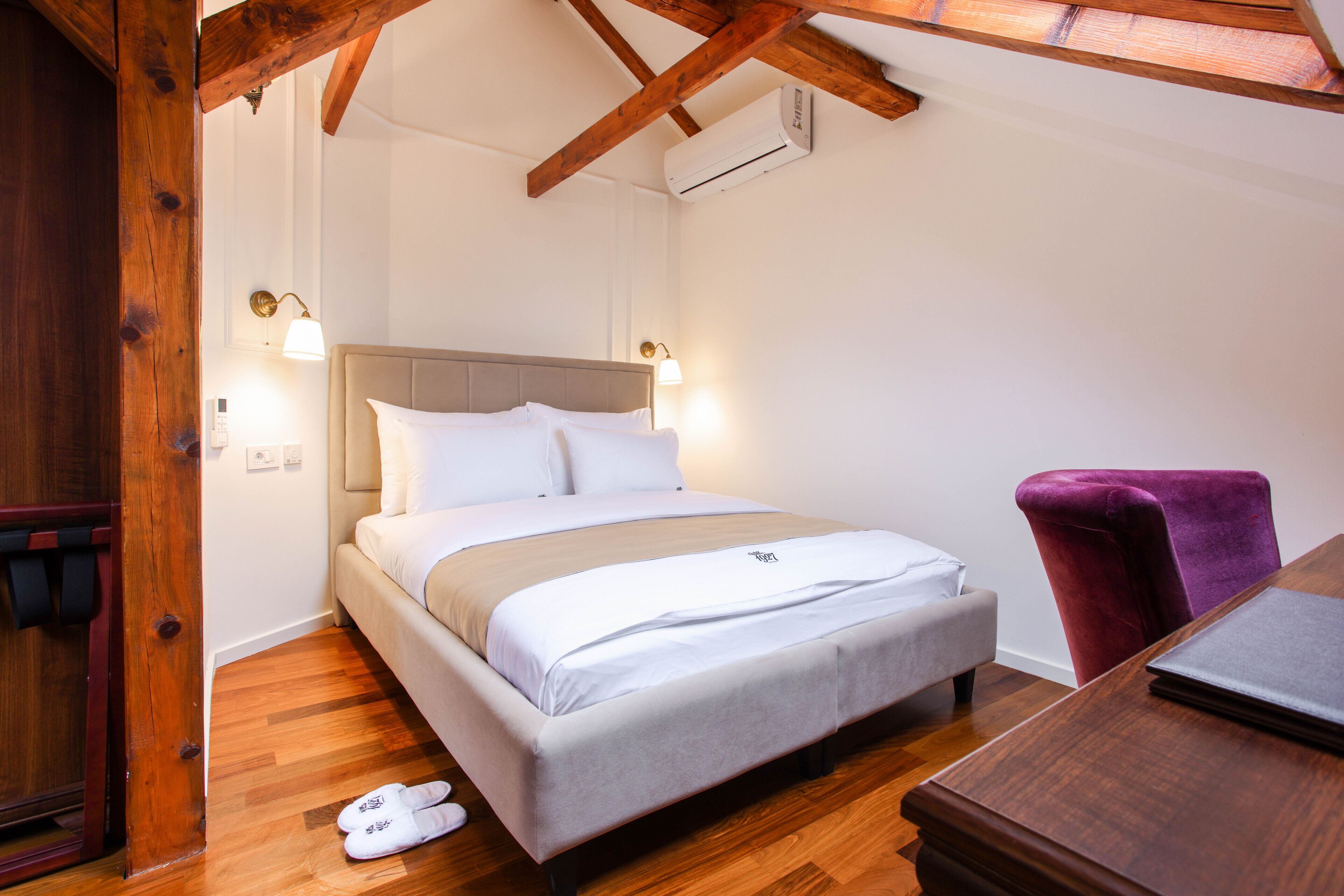 Un dormitorio con cama, piso de madera, un escritorio y una silla.