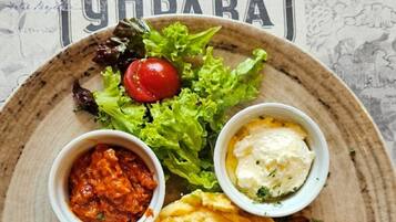 A plate with eggs, bacon, lettuce, a cherry tomato, and two small bowls of condiments.
