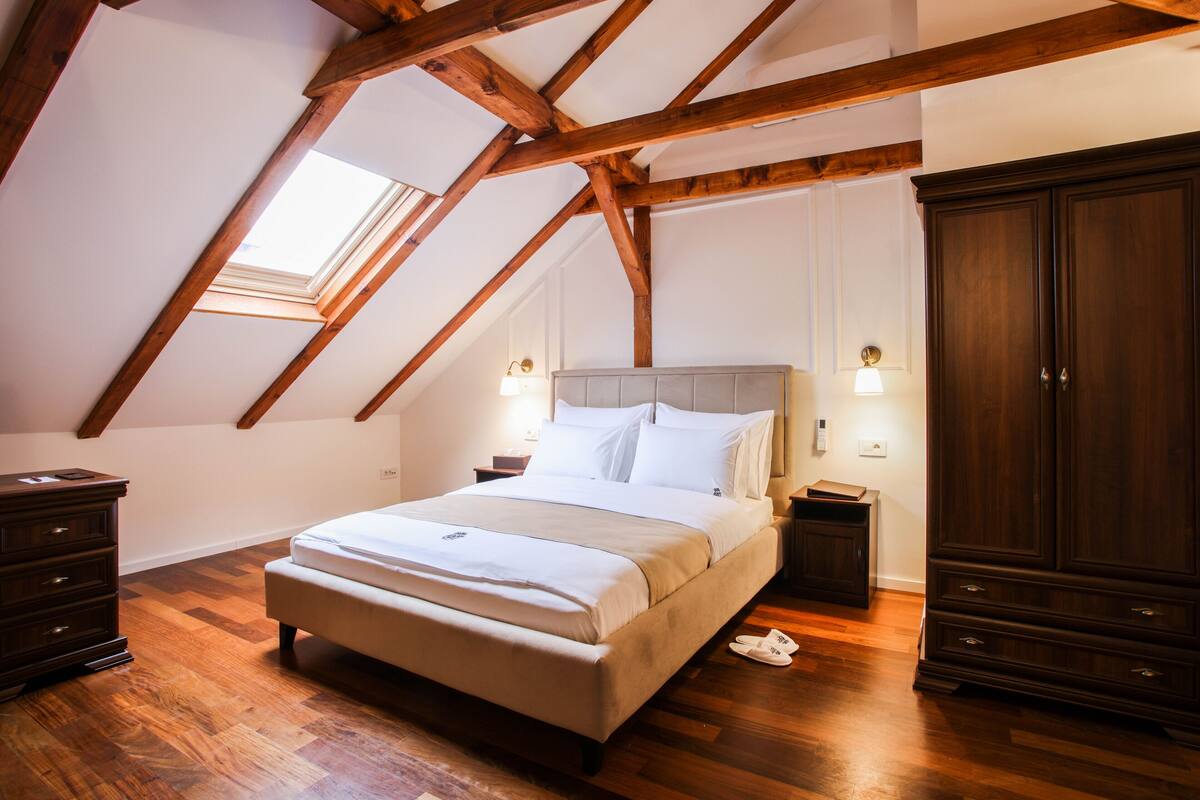 A bedroom with a sloped ceiling, a bed, a wardrobe, and a nightstand with a lamp.