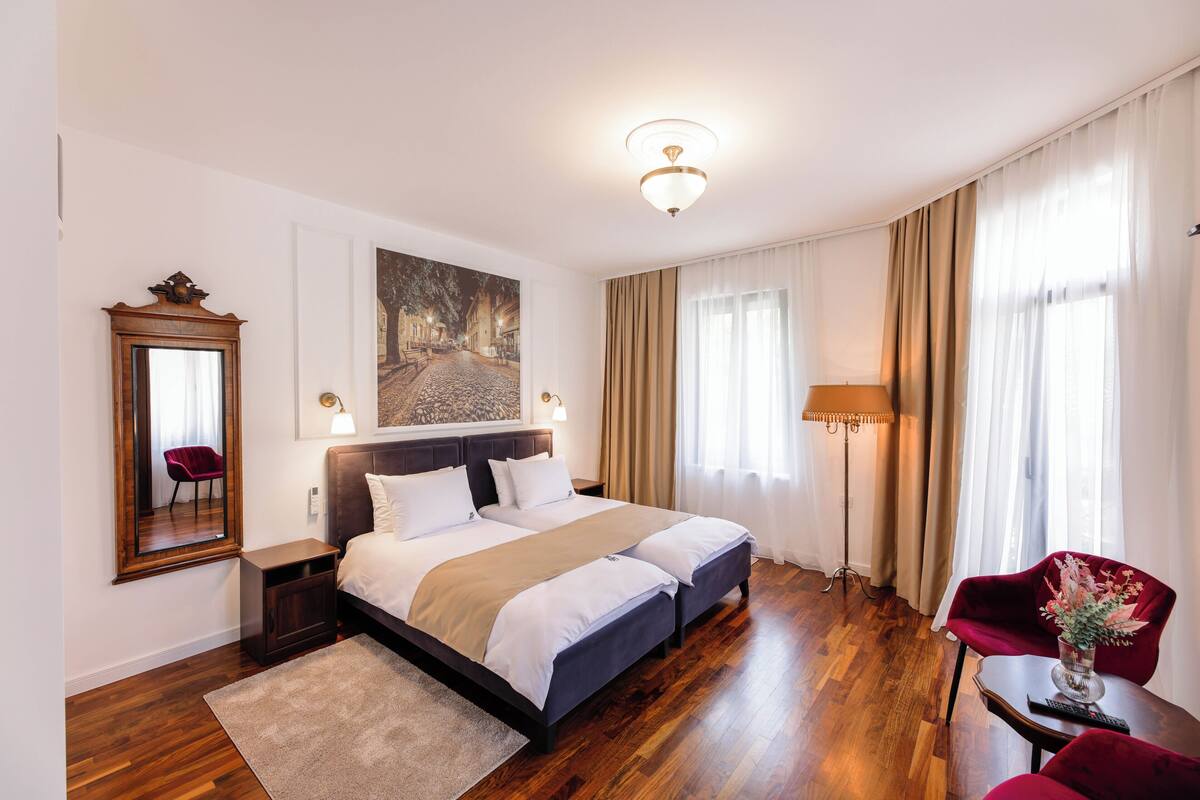 A hotel room with a large bed, a desk, a chair, a lamp, and a painting on the wall.