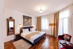 A hotel room with a large bed, a desk, a chair, a lamp, and a painting on the wall. - Villa 1927 (Belgrade)