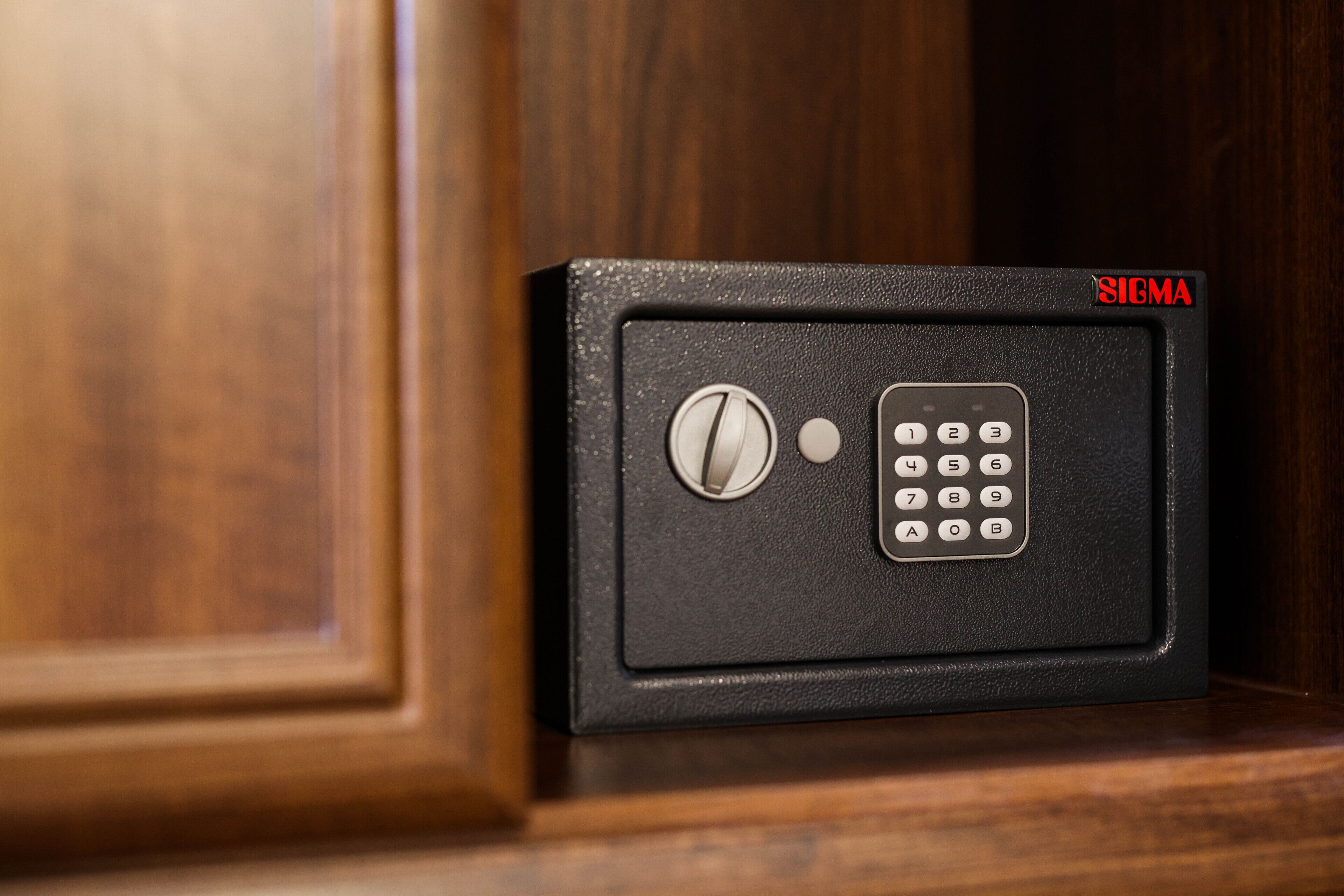 A black safe with a numeric keypad and a combination dial, labeled "SIGMA," placed against a wooden cabinet.