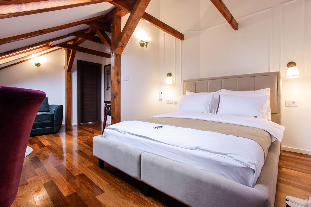 A bedroom with a large bed, wooden beams, and two wall-mounted lights.