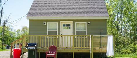 Ein zweistöckiges Haus mit Veranda, Grill und einem roten Stuhl.