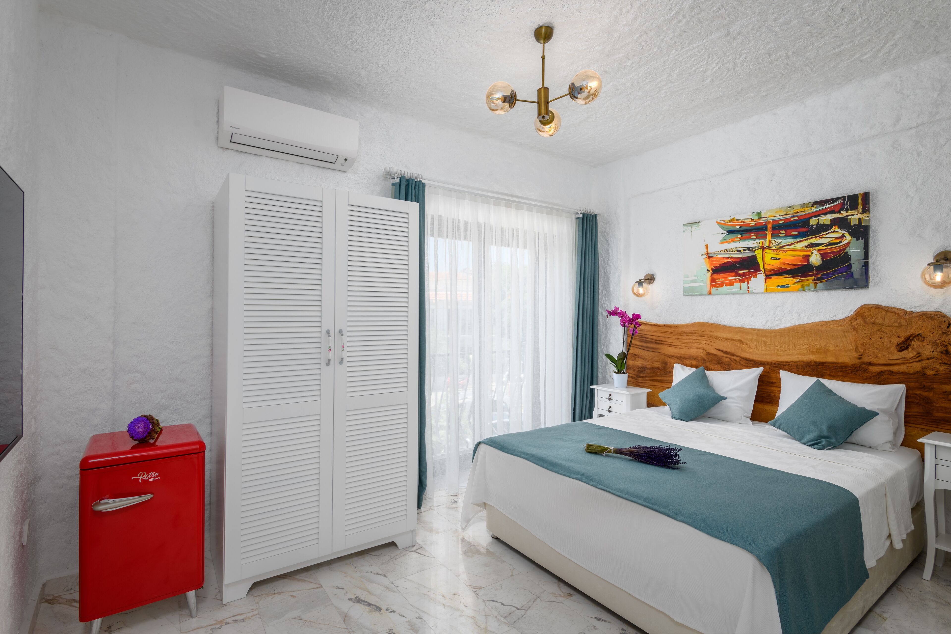 A bedroom with a bed, a red dresser, a wardrobe, and a painting on the wall.