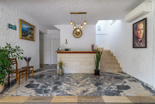 Um hall de hotel com piso de mármore, balcão de recepção, escadaria e um quadro na parede.