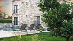 Un edificio de piedra con piscina y sillones de descanso.