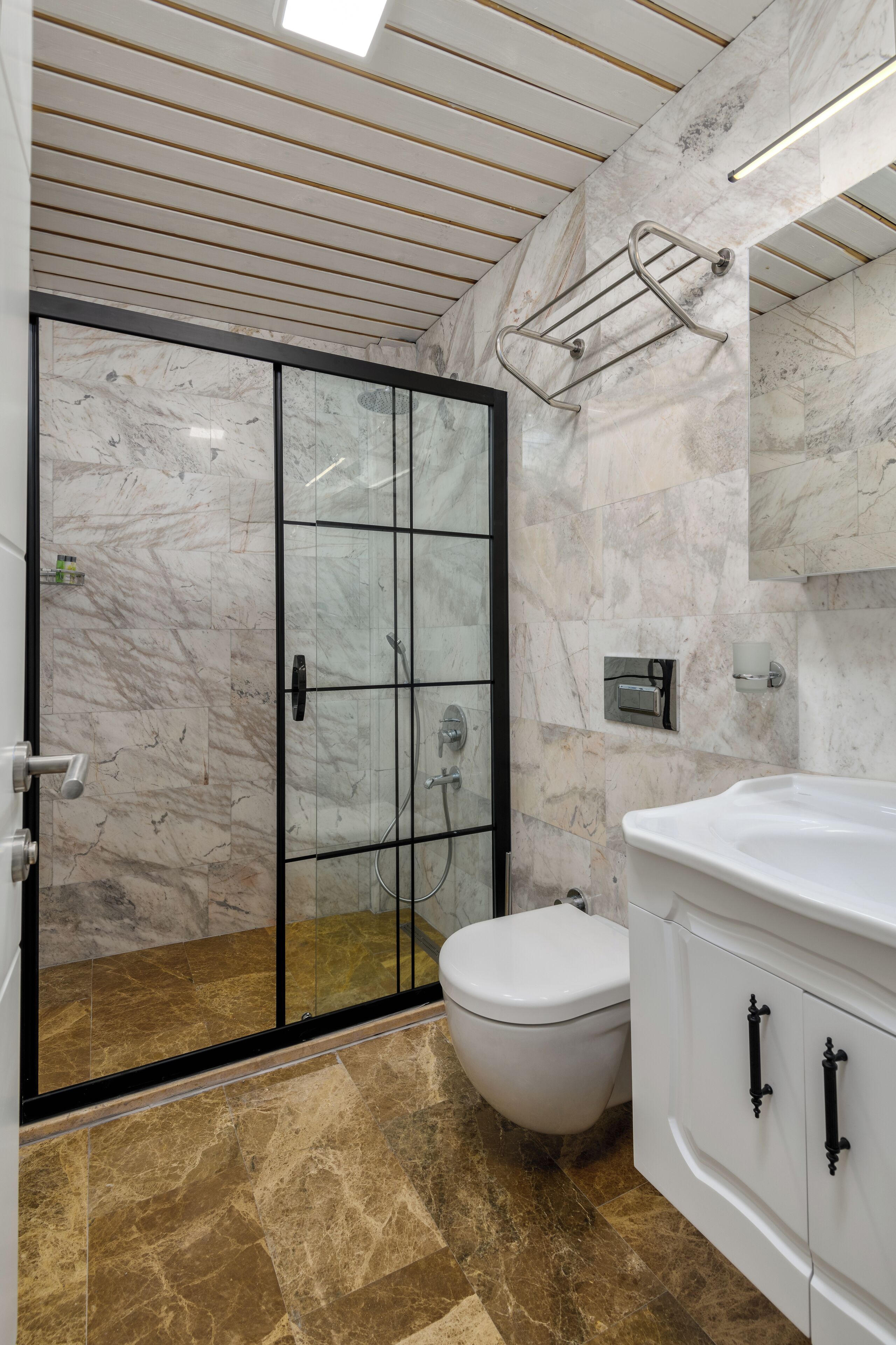 Un baño moderno con ducha envuelta en vidrio, inodoro blanco y pared revestida de mármol.