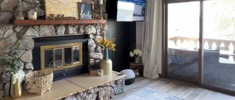 A living room with a stone fireplace, a flat-screen TV, and a large sliding glass door to the outdoors.