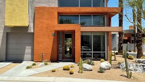 A modern two-story building with a glass entrance and a desert garden with cacti and rocks. - Modern Townhouse in Palm Springs (Palm Springs)